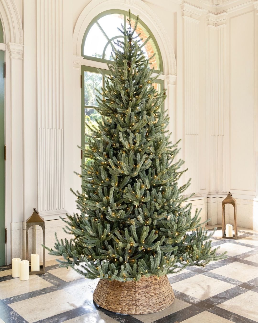 A beautifully decorated Balsam Fir Christmas tree in a large room with windows, creating a festive ambiance.