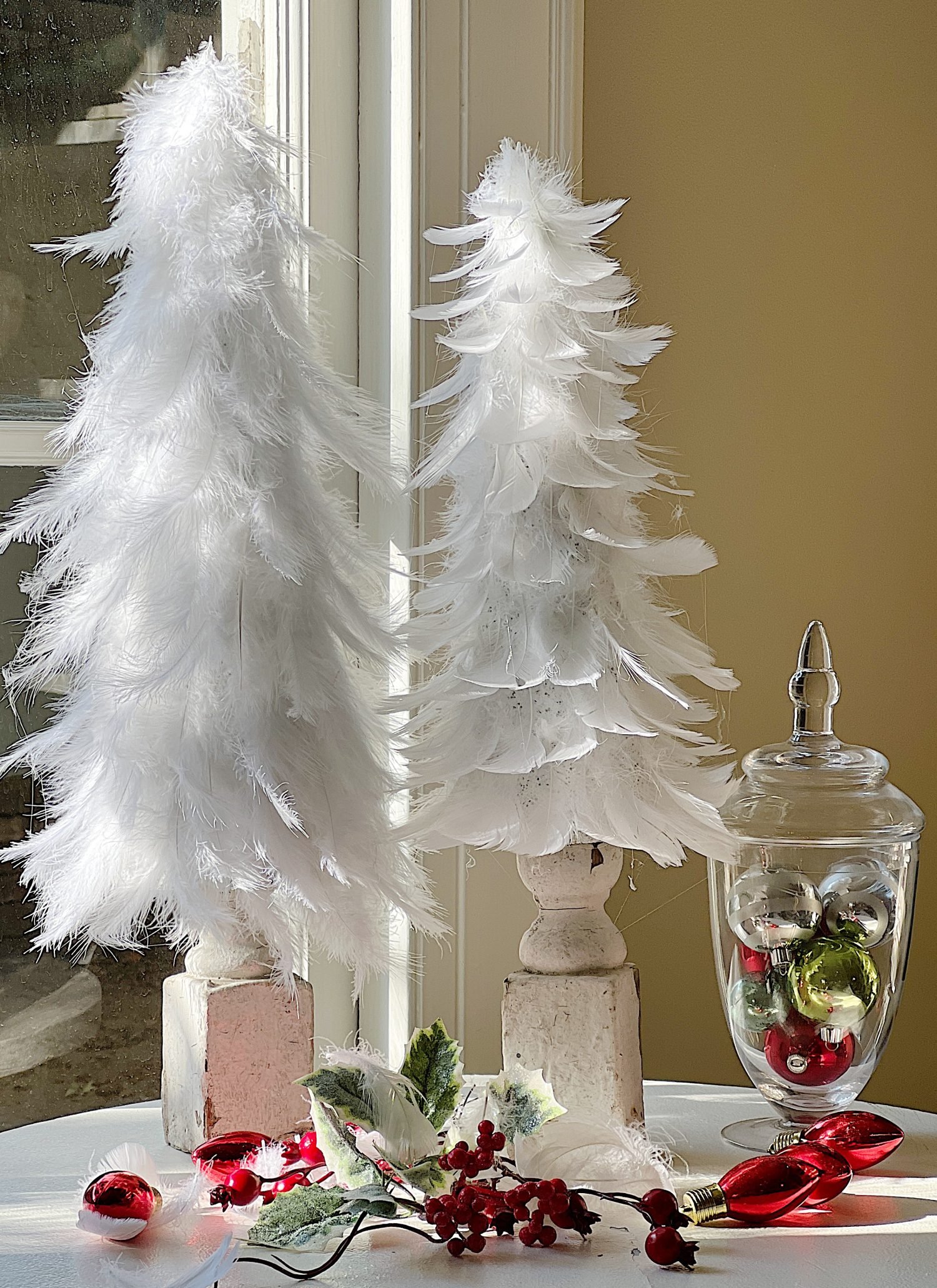 A table with two white Feather Trees and a vase.