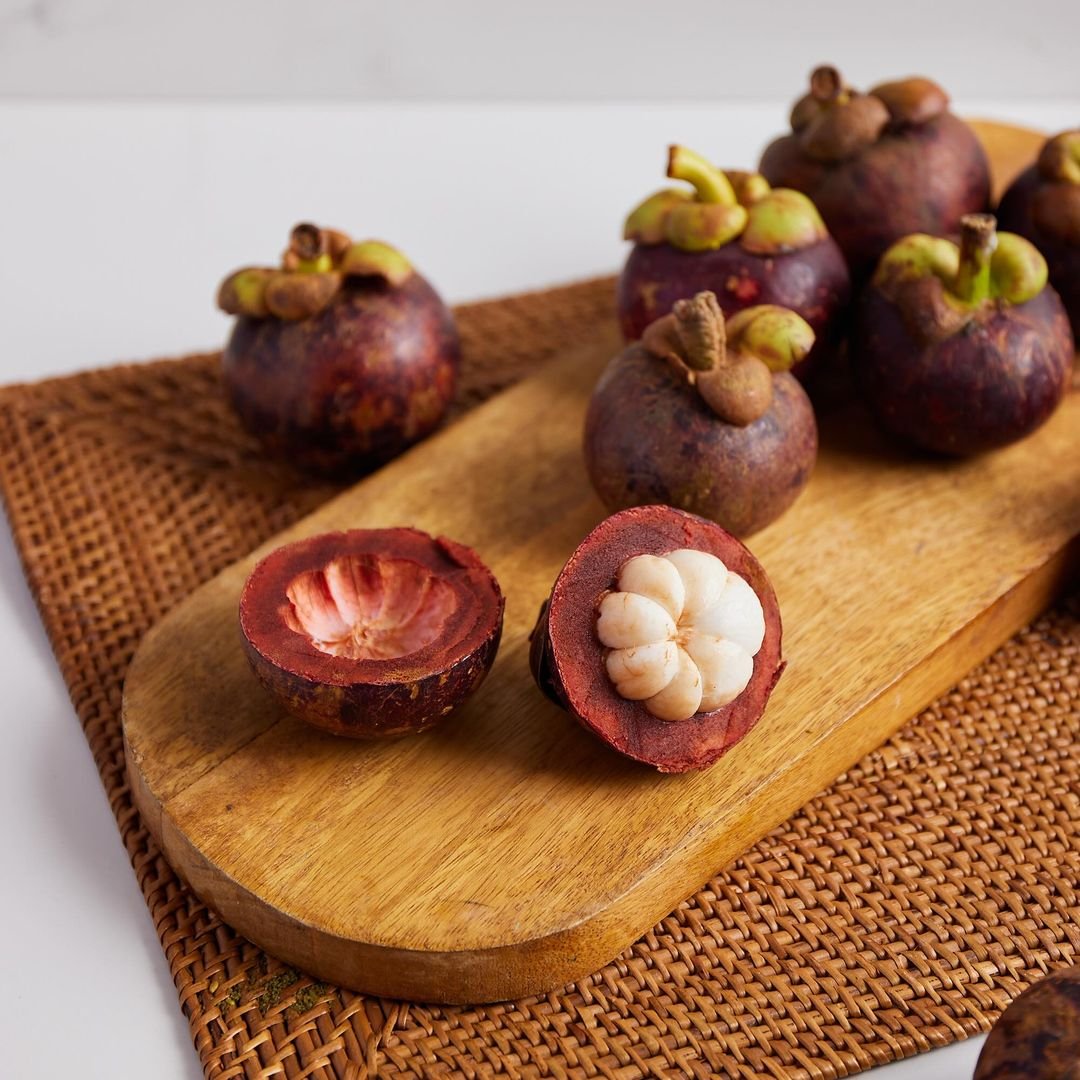 A wooden cutting board with ripe mangos, including mangosteen, ready to be sliced and enjoyed.

