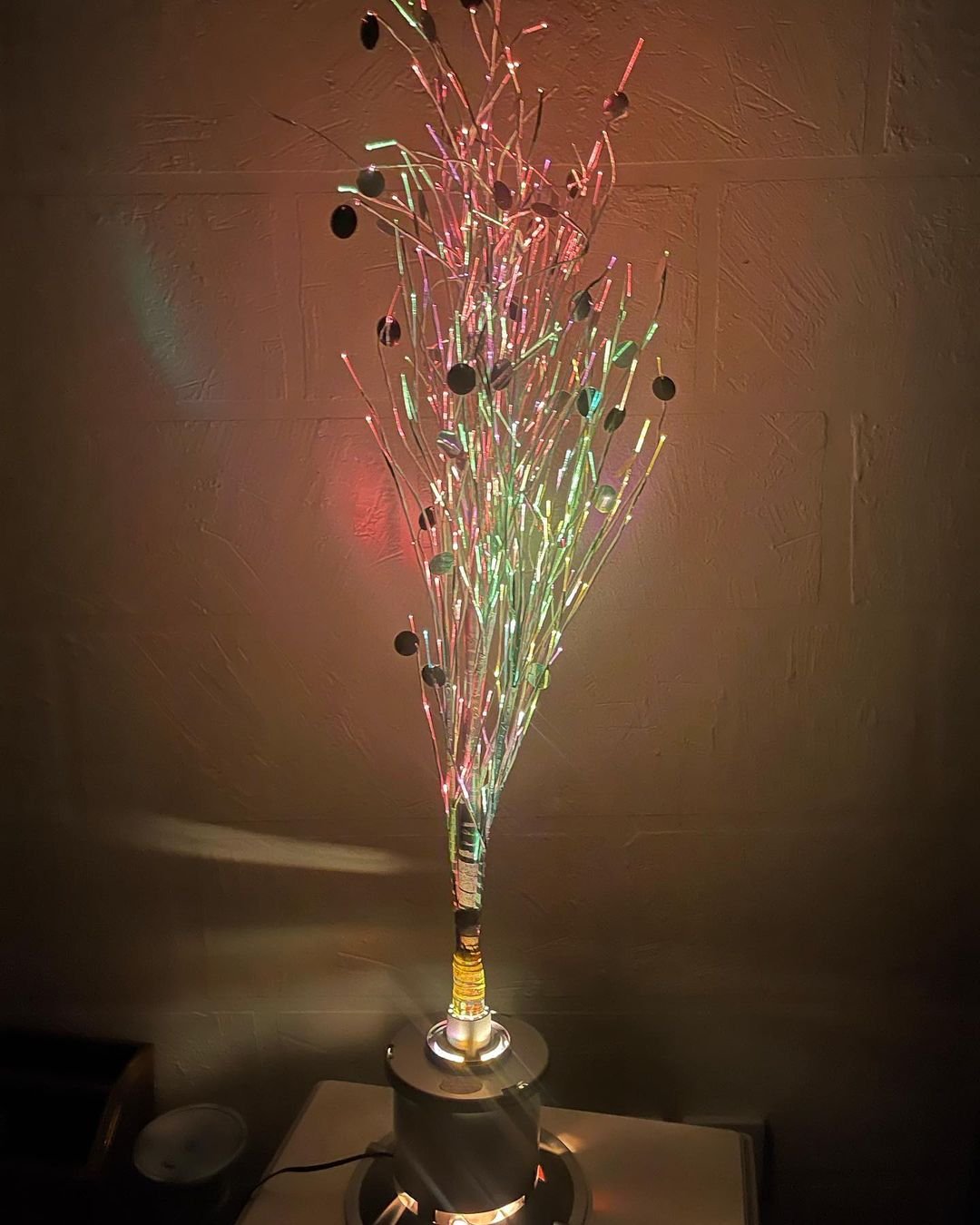 A vibrant vase with a champagne bottle, illuminated, accompanied by a Twig Tree.
