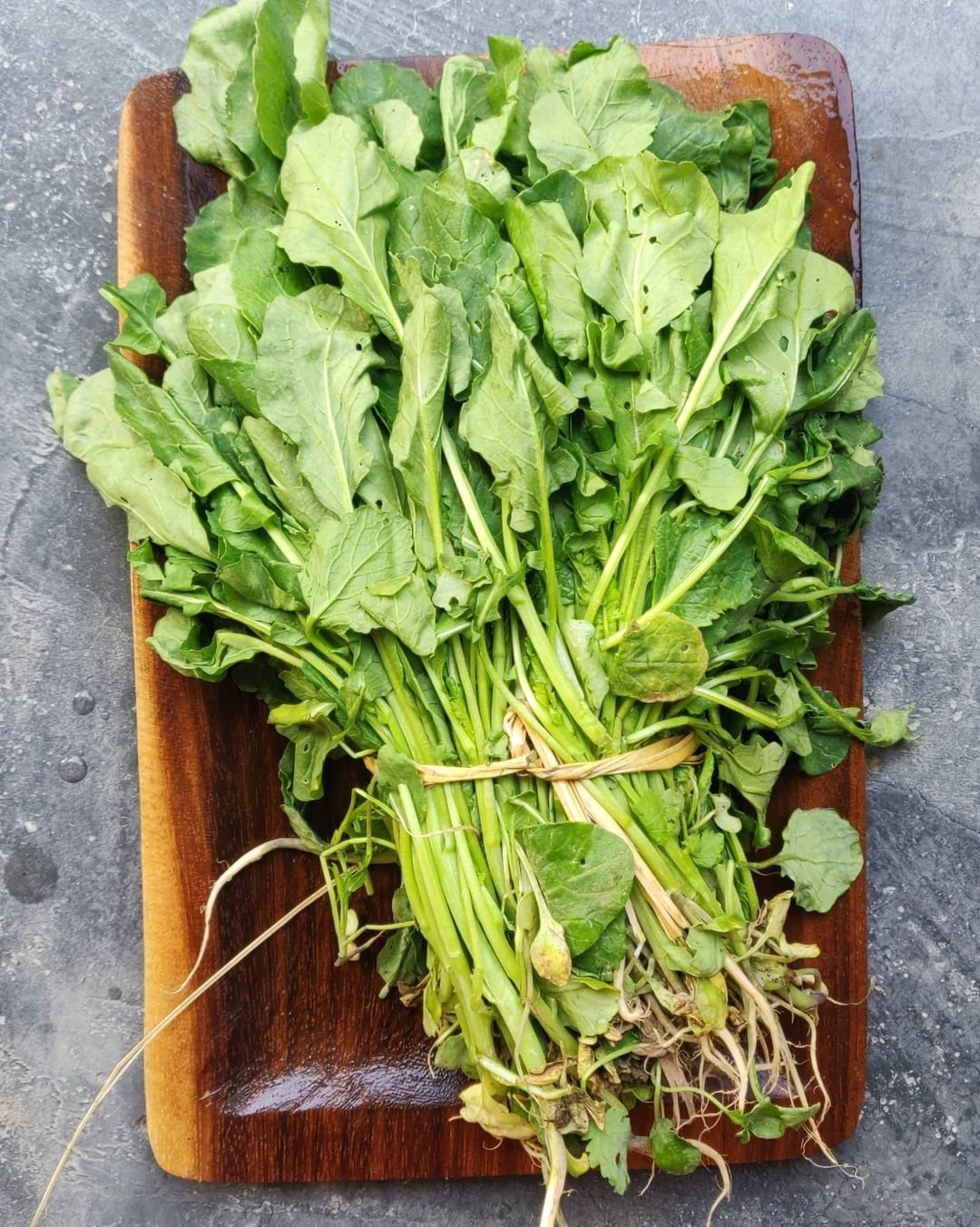 Fresh mustard greens on a wooden cutting board.