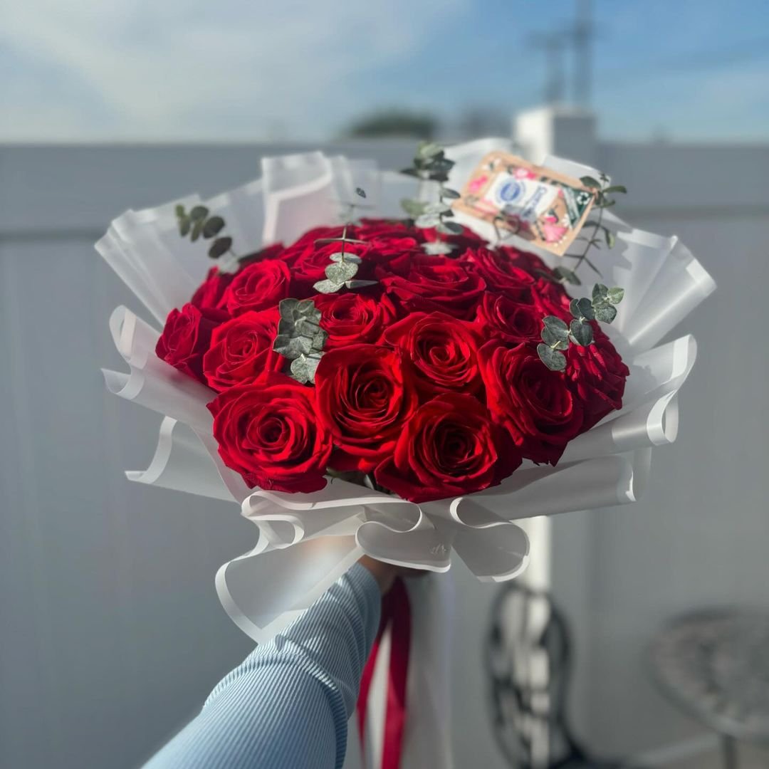 A person holds a round bouquet of vibrant red roses in their hand, showcasing the beauty of the flowers.
