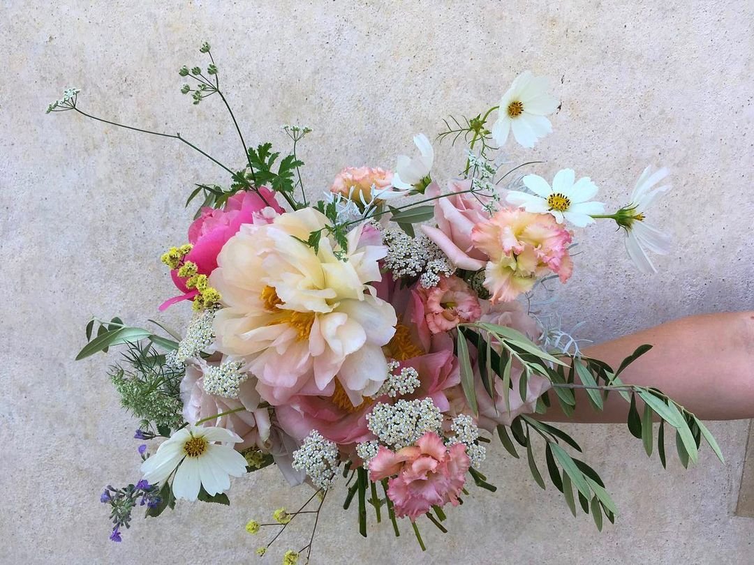 A person gracefully holds a vibrant Tuscan bouquet, showcasing an array of colorful flowers in a serene setting.