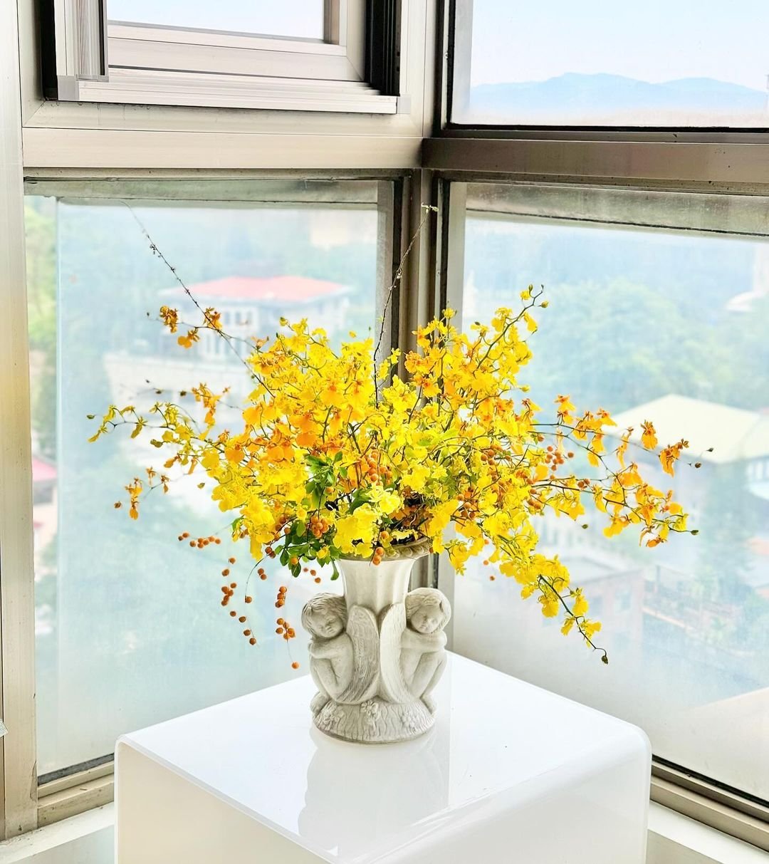 A vase filled with vibrant yellow flowers placed on a table, illuminated by natural light from a nearby window.
